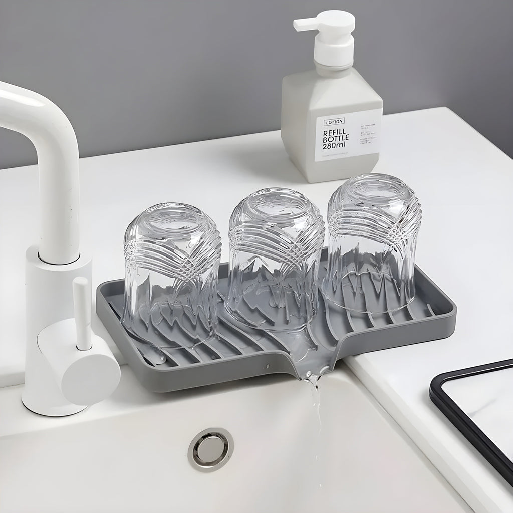 HomeShape grey silicone draining tray holding three inverted glass cups on a white bathroom sink countertop