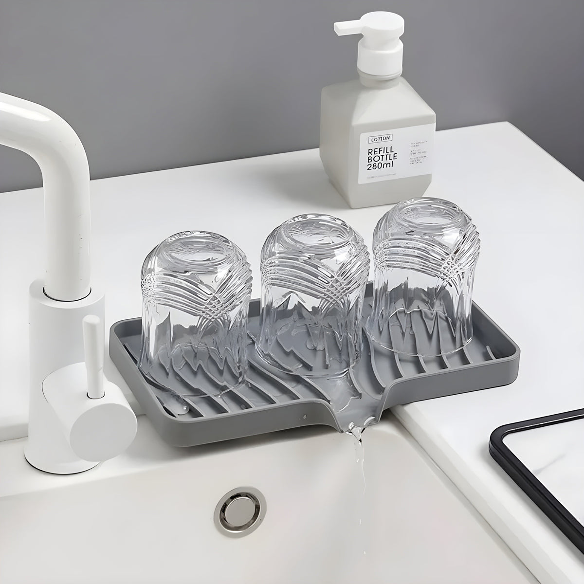 HomeShape grey silicone draining tray holding three inverted glass cups on a white bathroom sink countertop